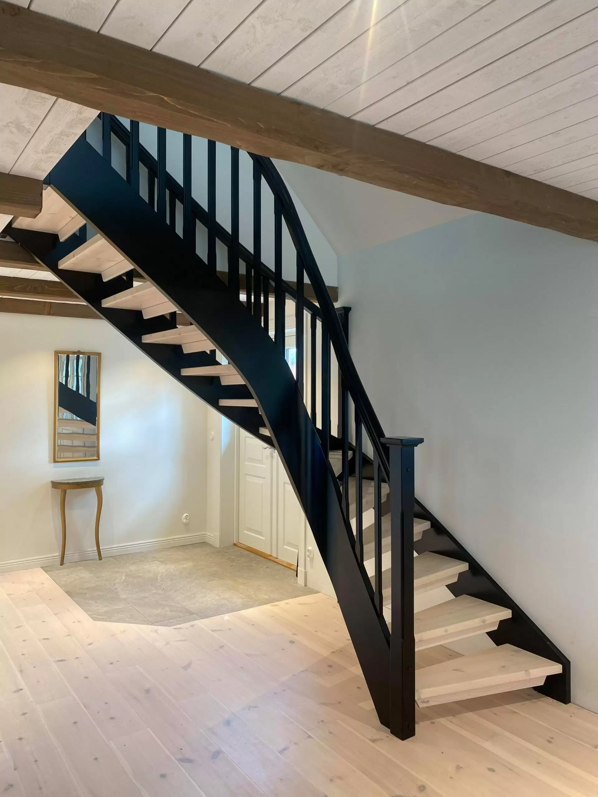 ljusa trästeg i svängd trappa med svart räcke