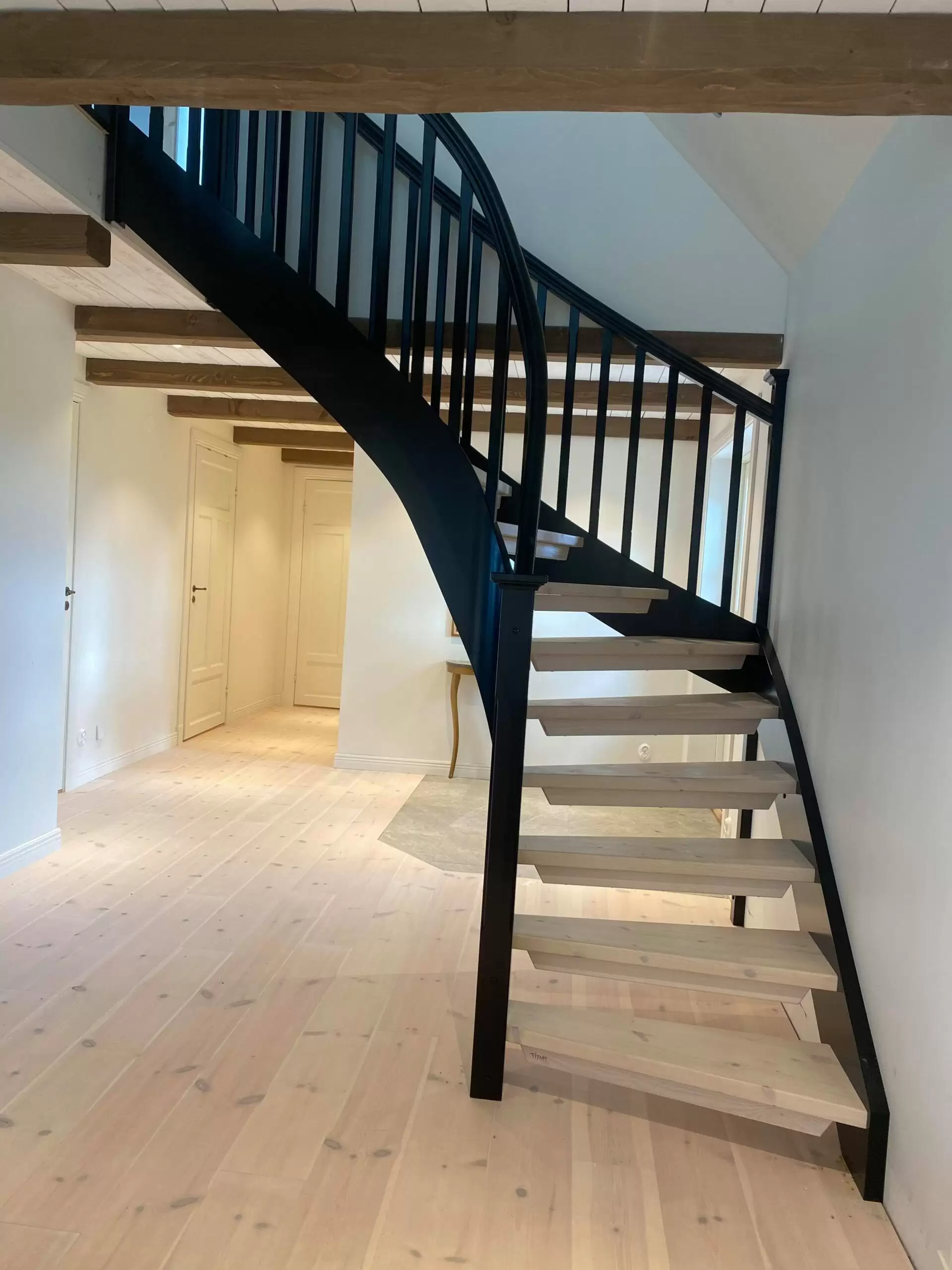 ljus parkett som följer med i trappstegen, trappa med svart räcke